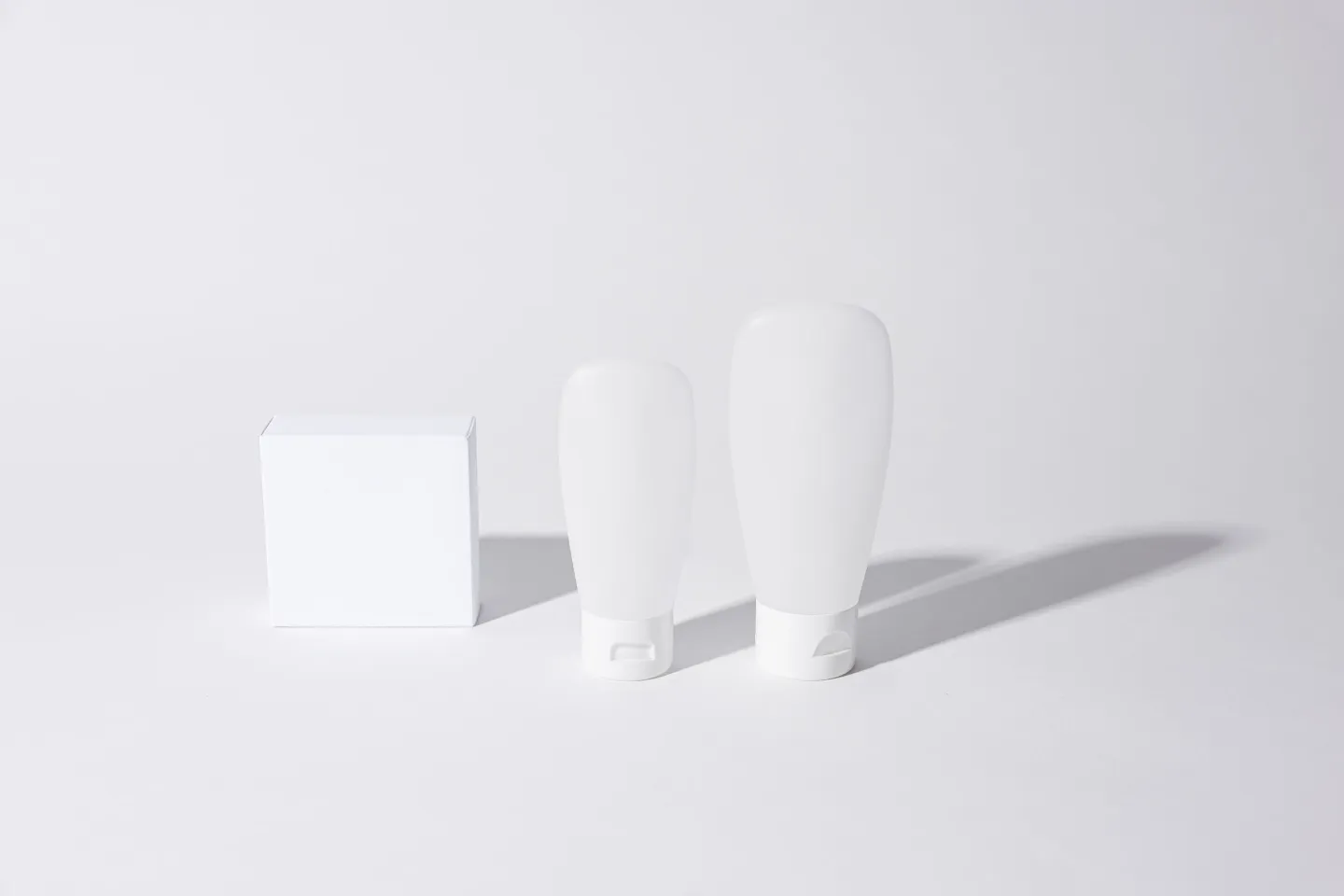 Two blank white cosmetic tubes and a plain white box on a white surface.