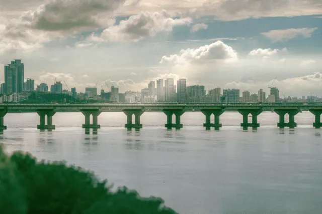 Seoul's skyline across the Han River, with a long road bridge in the foreground.