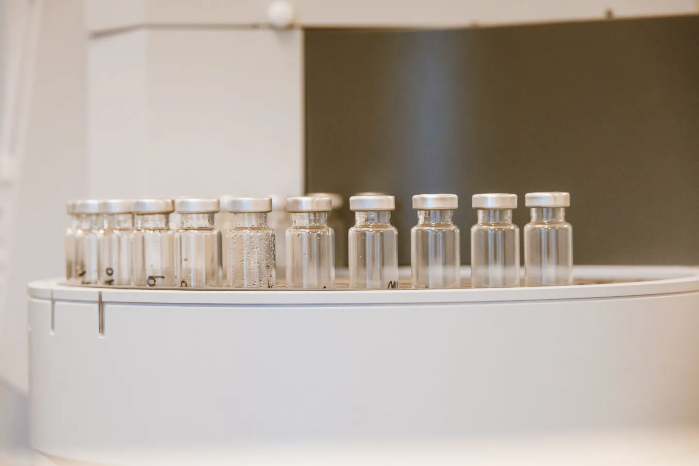 A row of small empty glass vials with metal caps on a white laboratory instrument.