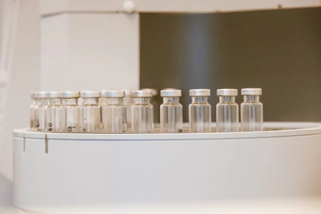 A row of small empty glass vials with metal caps on a white laboratory instrument.