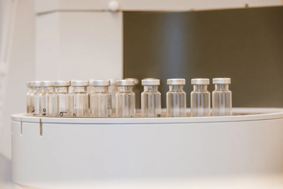 A row of small empty glass vials with metal caps on a white laboratory instrument.